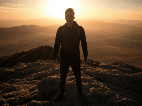 Person standing on a mountain at sunrise, symbolizing success.